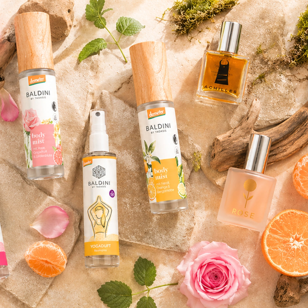 Flatlay mit Baldini Bodymist, Yogaduft, Achilles und Rose Parfum auf Sandstein mit Rosenblüten und Orangen – Naturdüfte erhältlich im dieNikolai Sortiment