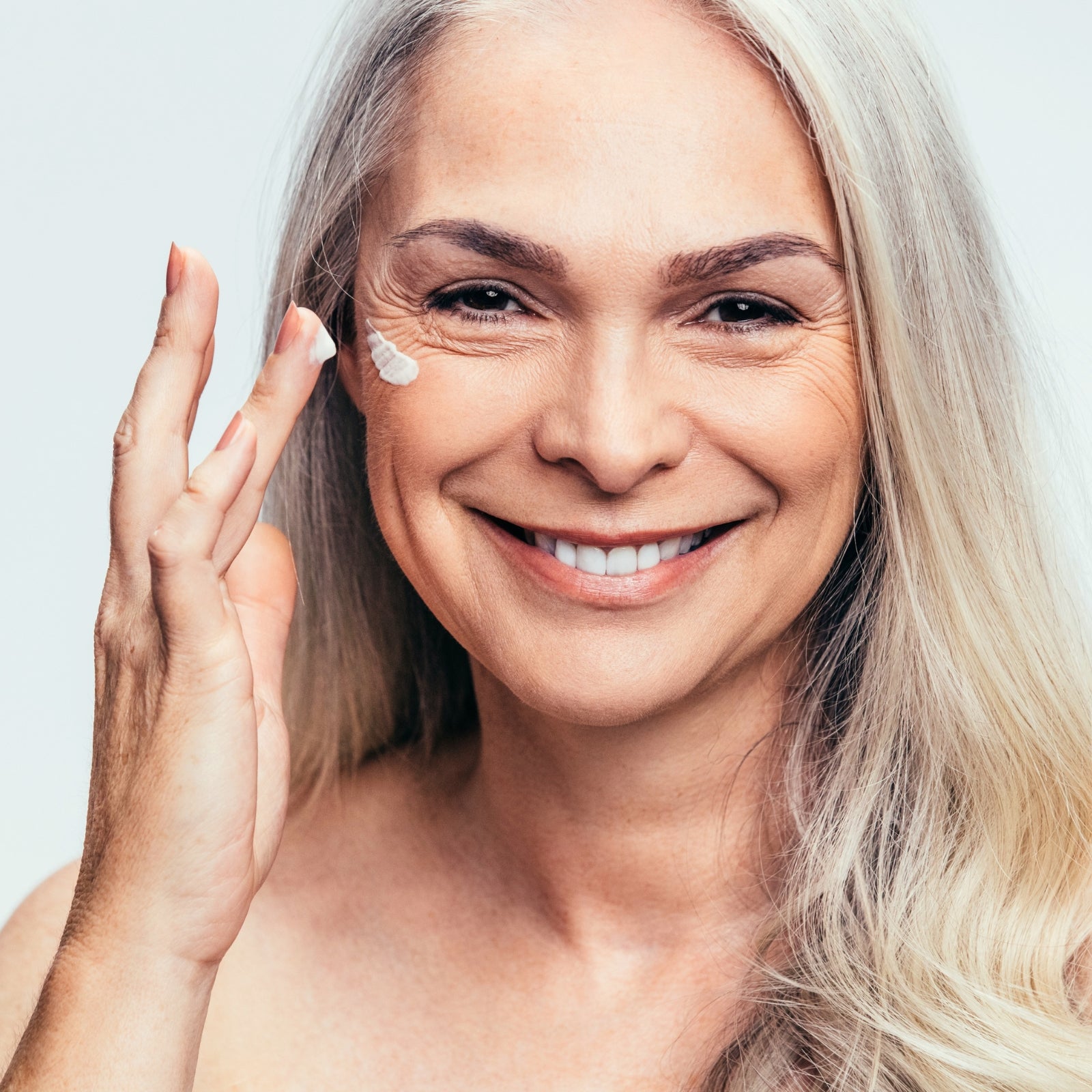 Strahlende Frau im besten Alter mit silbergrauem Haar trägt Pflegecreme auf die Wange auf – natürliche Anti-Aging-Pflege mit dieNikolai Demeter Bio-Traubenkosmetik aus der Wachau
