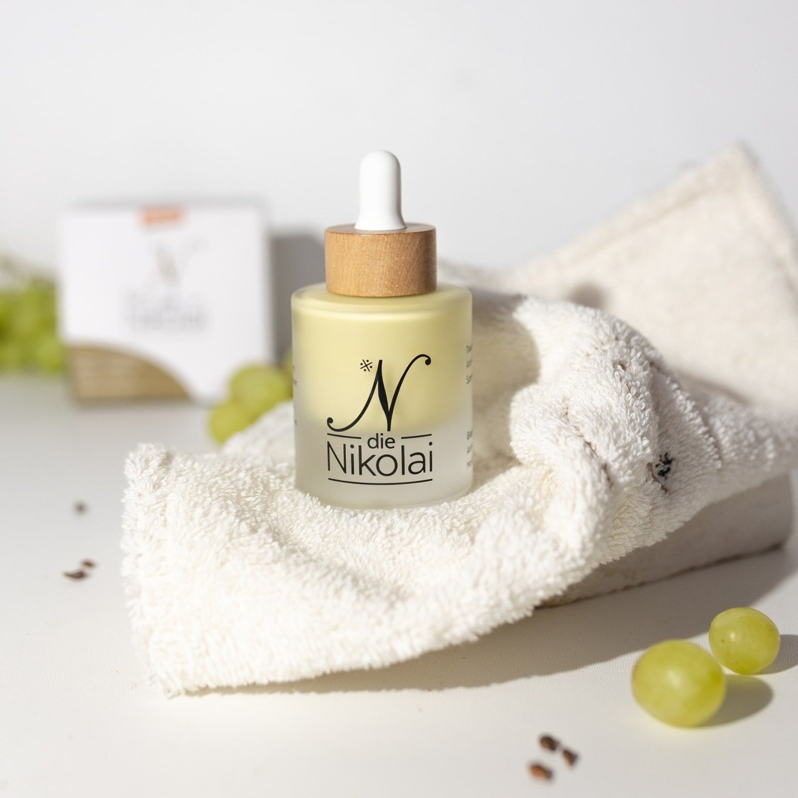 Pipettenflasche dieNikolai Intensiv-Serum auf cremigem Frotteetuch mit Weintrauben und Traubenkernen – Demeter Bio-Traubenkosmetik aus der Wachau