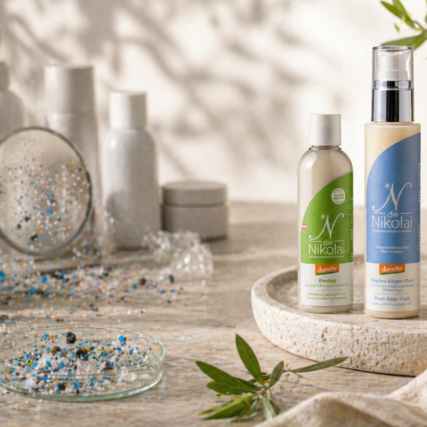 dieNikolai Riesling Duschgel und Frisches Körper-Fluid mit Demeter-Siegel neben Glasschalen mit Mikroplastik – mikroplastikfreie Bio-Traubenkosmetik aus der Wachau