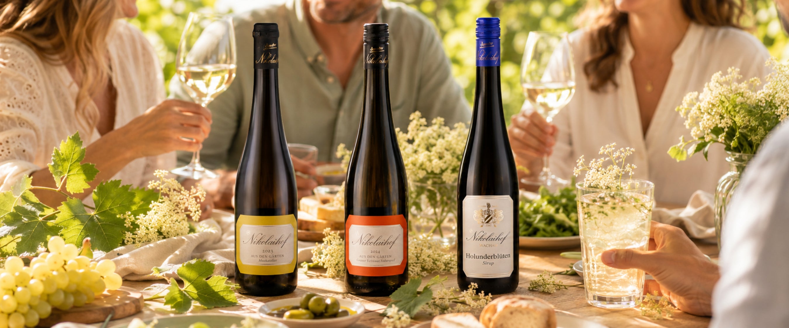 Sommerliche Tafel mit Nikolaihof Wachau Weinen, Holunderblüten-Sirup, Trauben und Brot – kulinarisches Erbe hinter dieNikolai Bio-Traubenkosmetik aus Österreich