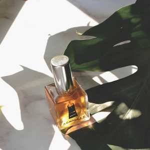 Goldenes Parfum-Flakon mit Silberdeckel im Sonnenlicht auf Marmor mit Monstera-Blatt – exklusiver Duft im dieNikolai Sortiment, Bio-Naturkosmetik