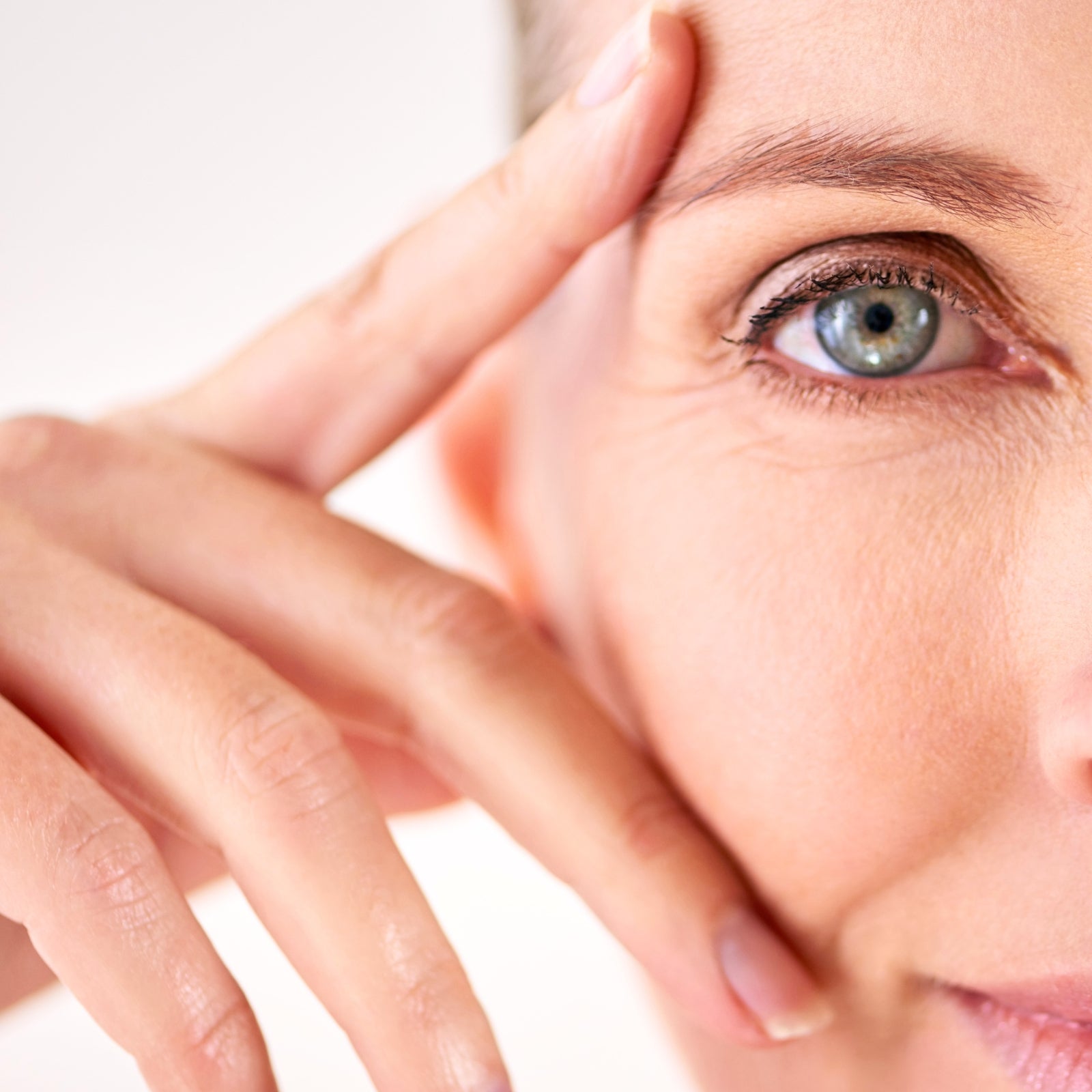 Nahaufnahme eines hellen Frauenauges, Finger berührt sanft die Augenpartie – Anwendung des dieNikolai Augen-Serums aus Demeter Bio-Traubenkosmetik aus der Wachau