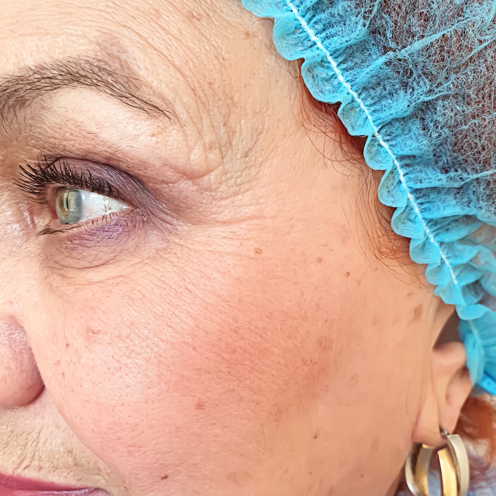 Detailaufnahme eines reifen Frauenauges mit Mascara und blauer OP-Haube – Anwendungsbeispiel für die Augenpflege mit dieNikolai Demeter Bio-Traubenkosmetik aus der Wachau