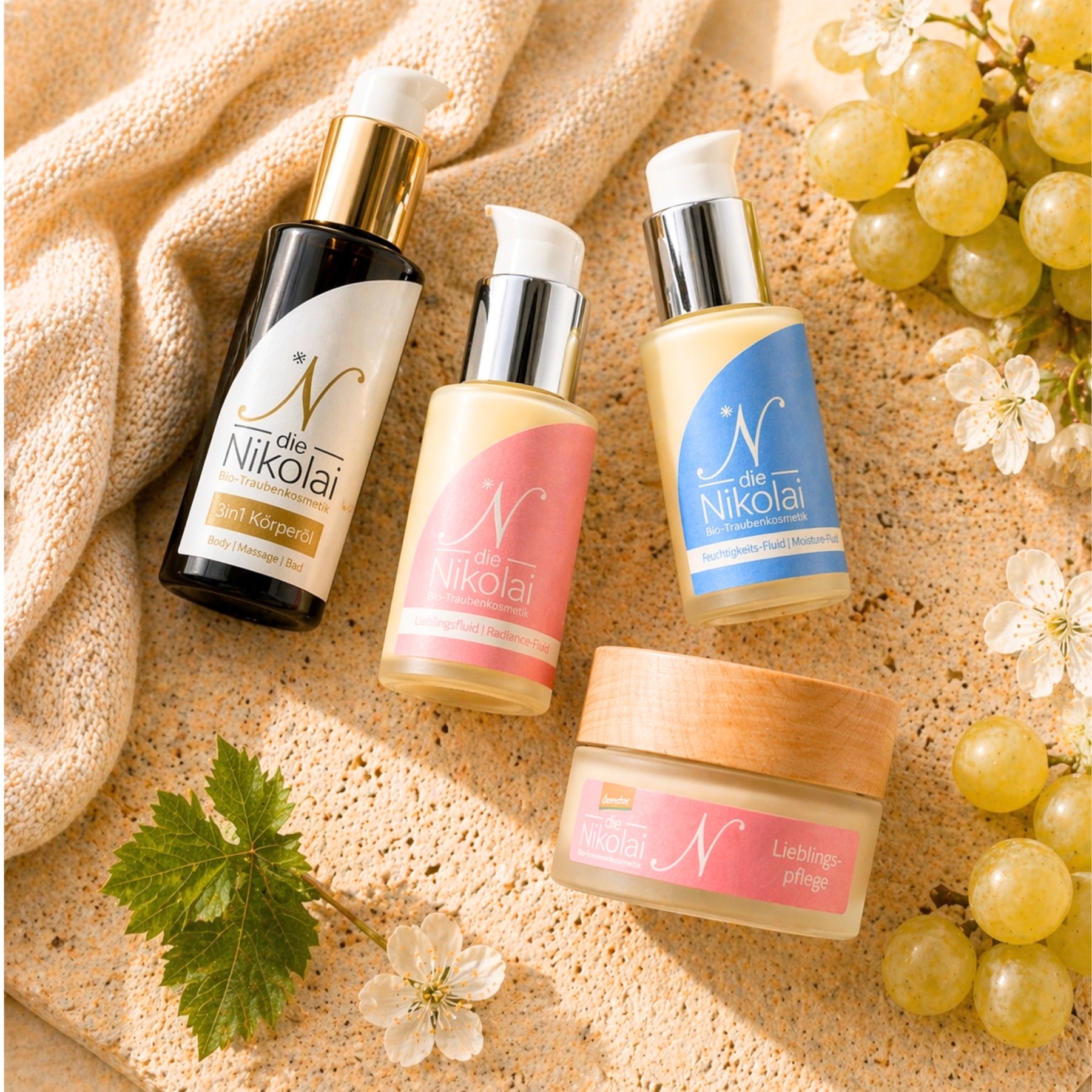 Flatlay mit dieNikolai Sanftem Körperöl, Lieblingsfluid, Lieblingspflege-Tiegel und Augenpflege auf Decke mit Trauben – Demeter Bio-Traubenkosmetik aus der Wachau