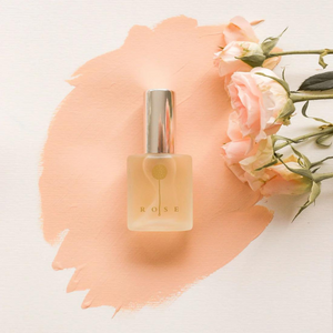 Lakshmi Rose Naturparfum Glasflakon auf pfirsichfarbenem Pinselstrich mit Rosenblüten – ayurvedischer Bio-Duft im dieNikolai Sortiment
