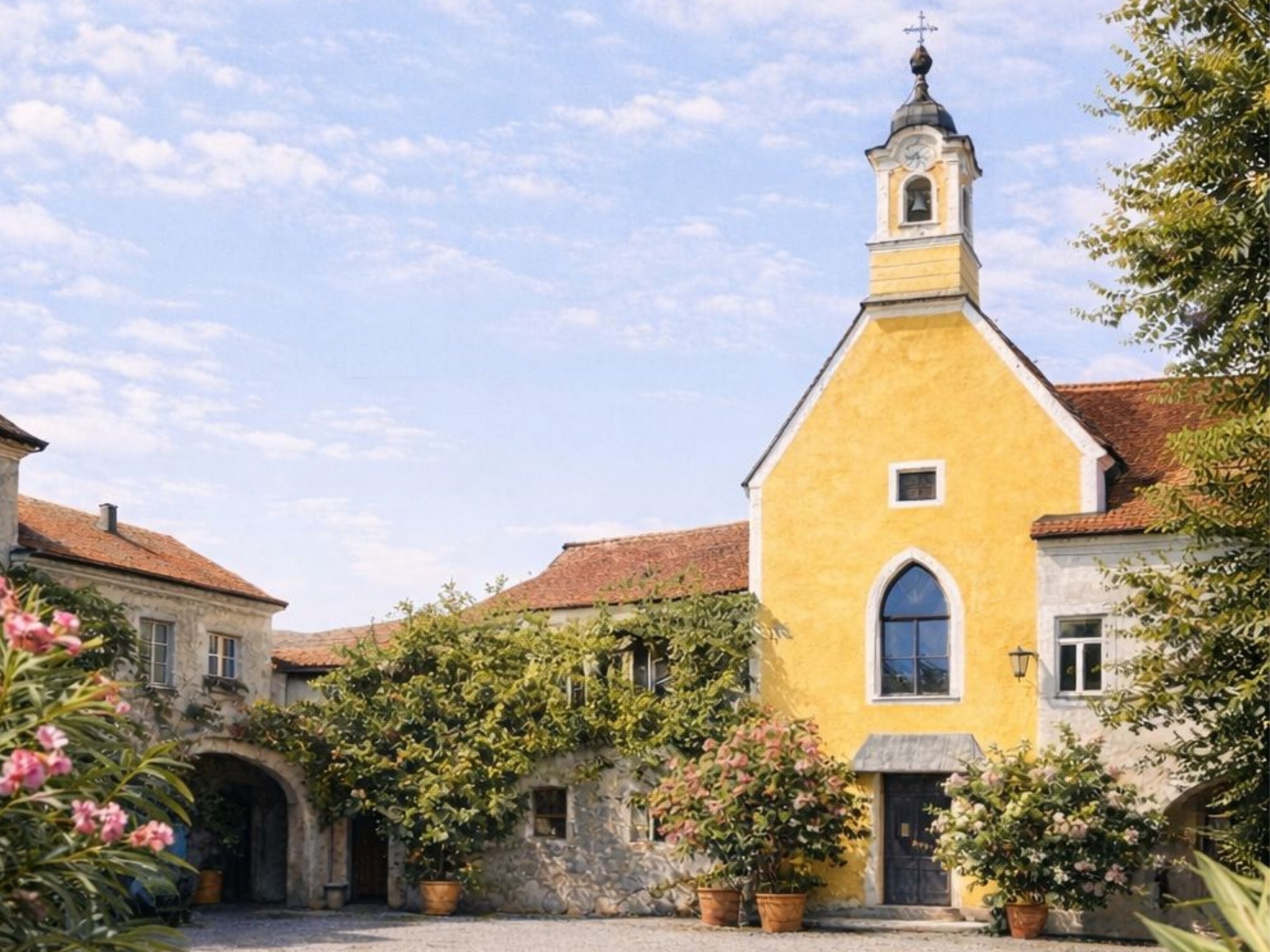Idyllischer Innenhof des Nikolaihofs in der Wachau mit gelber Kapelle, rosa Oleander und Glockenturm – historische Heimat der dieNikolai Demeter Bio-Traubenkosmetik