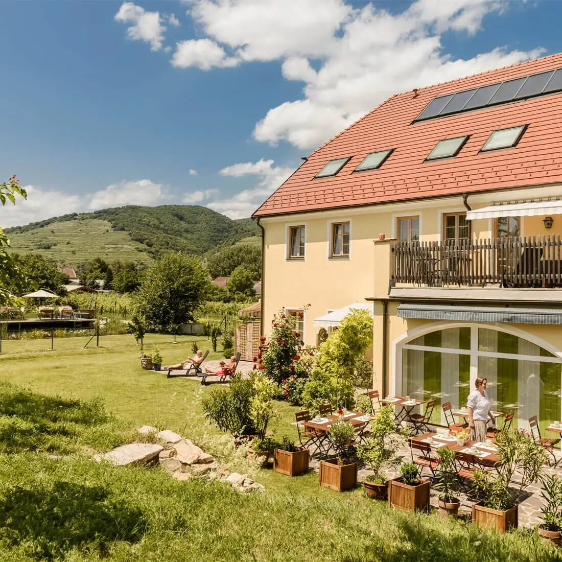 Sonniger Blick auf das Gästehaus des Nikolaihofs Wachau mit Terrasse, Liegestühlen und Hügeln im Hintergrund – Heimat der dieNikolai Bio-Traubenkosmetik aus Österreich
