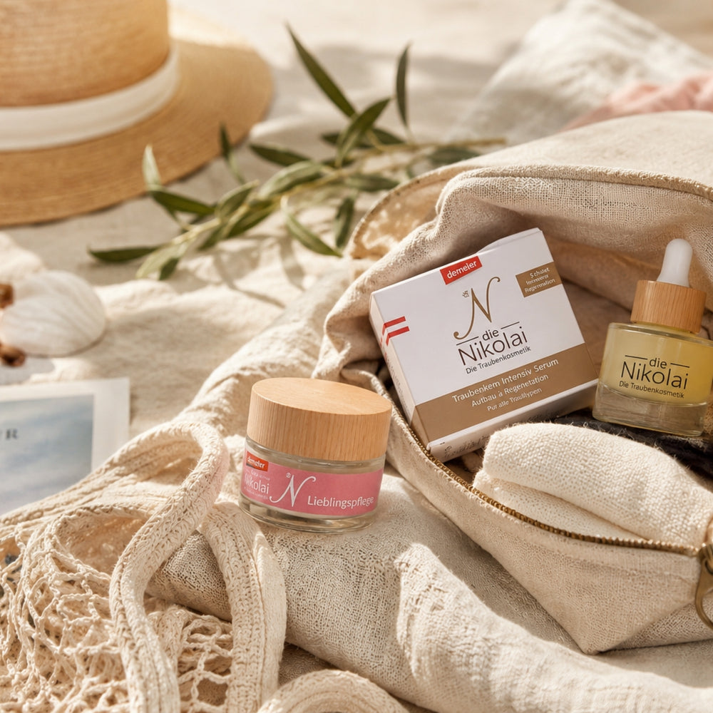 Strohhut, Olivenzweig und Postkarte mit dieNikolai Lieblingspflege, Intensiv-Serum und Traubenkernöl auf weichem Tuch – sommerliche Demeter Bio-Traubenkosmetik aus der Wachau