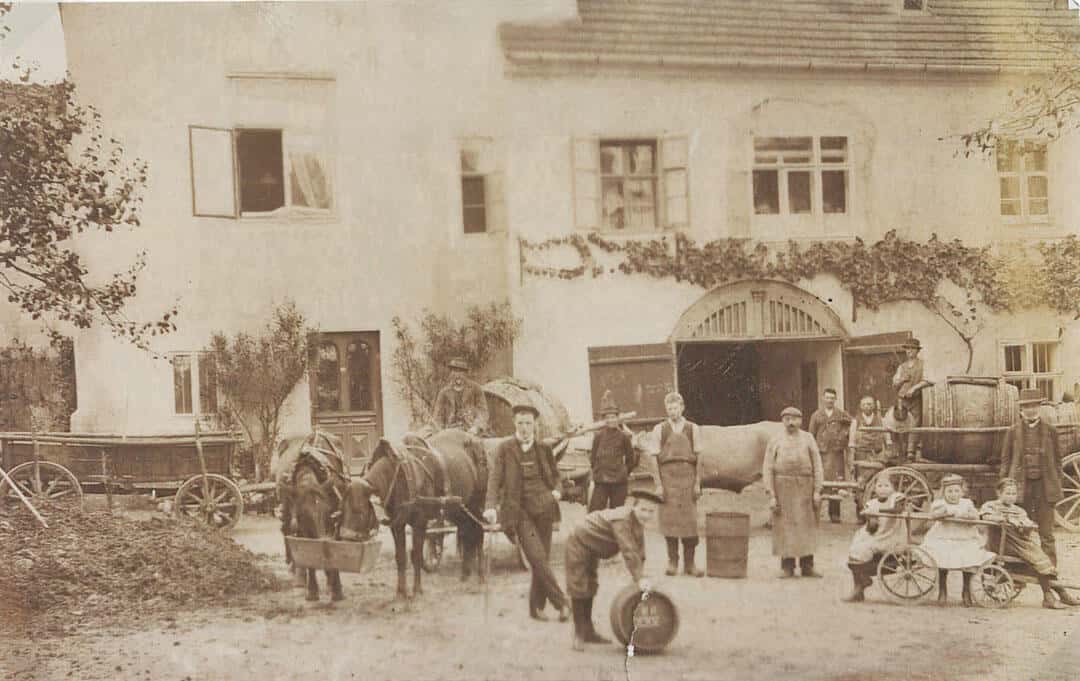 Historisches Sepia-Foto vor dem Nikolaihof Wachau mit Pferdefuhrwerken, Weinküfern und Familie – Tradition hinter dieNikolai Bio-Traubenkosmetik aus Österreich